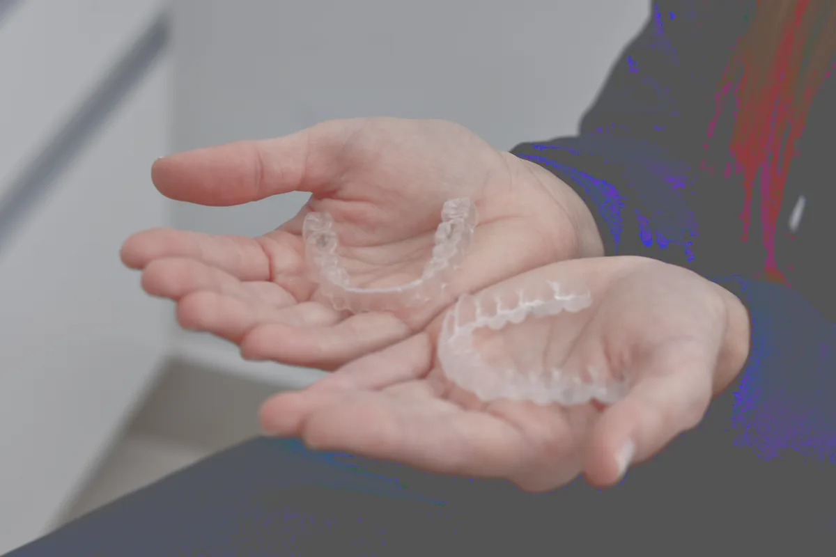 Two clear aligner trays held in open hands, graded.